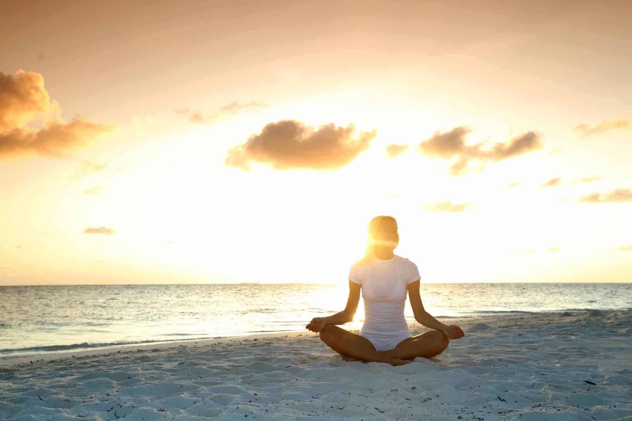 Woman meditating on the beach at sunrise