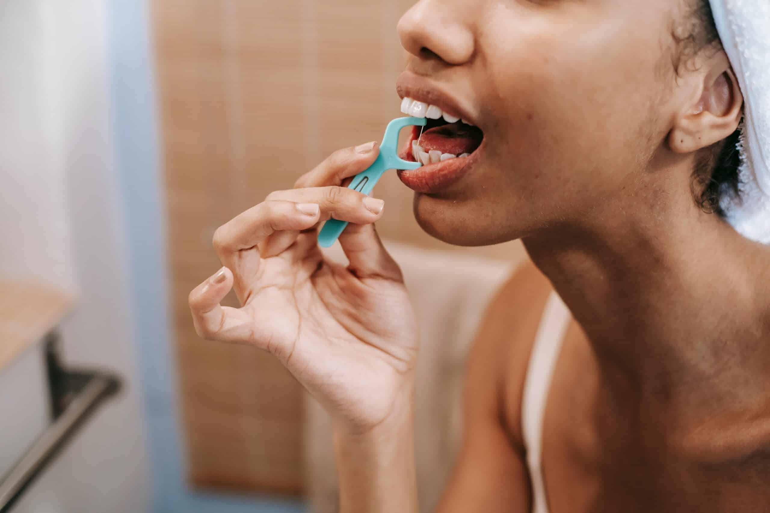 Woman demonstrating the benefits of flossing by carefully cleaning between her teeth for a healthy smile.