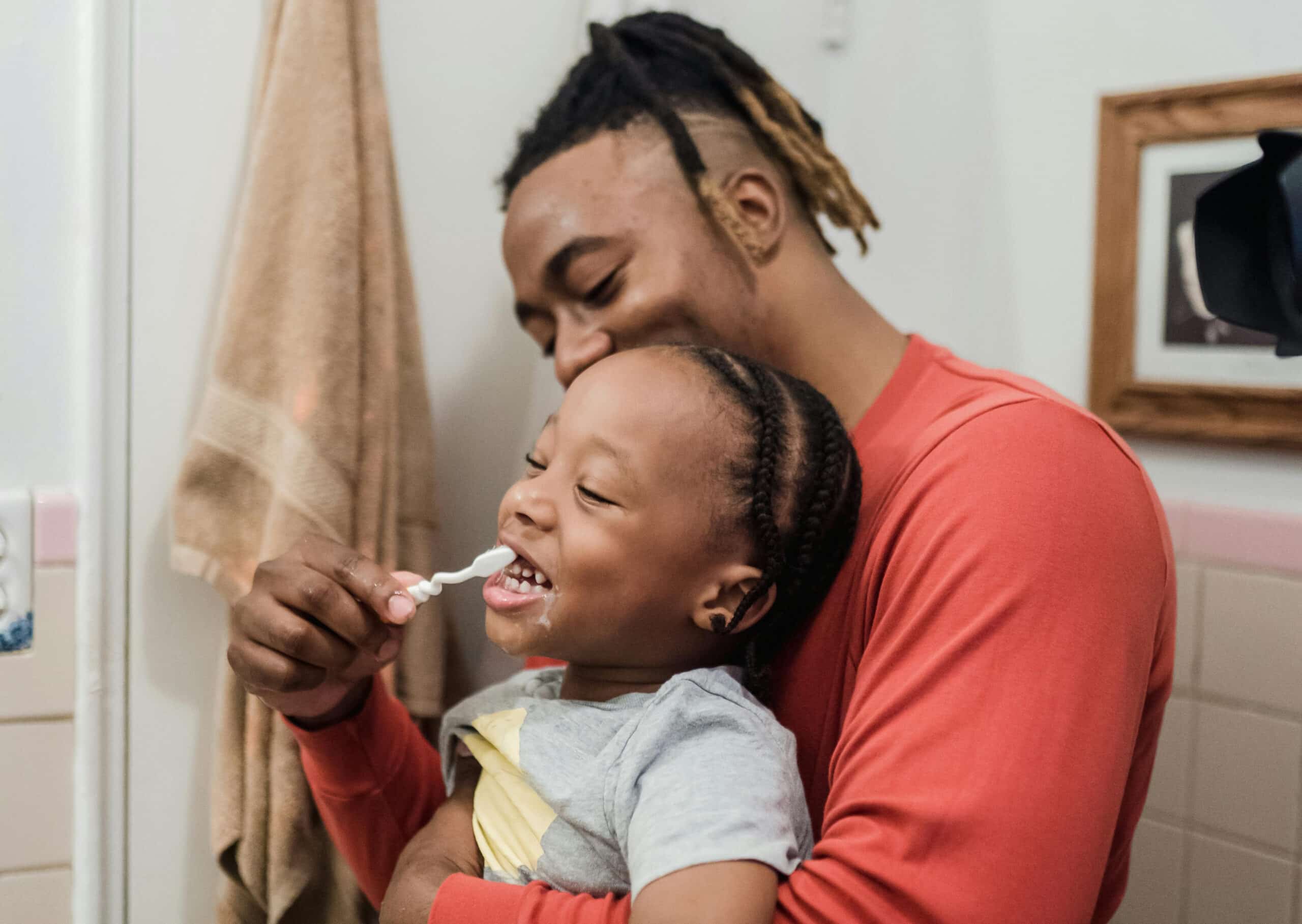 A dad helping his child brush their teeth before or after breakfast