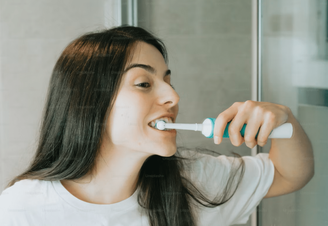 A woman brushing her teeth with an electric toothbrush