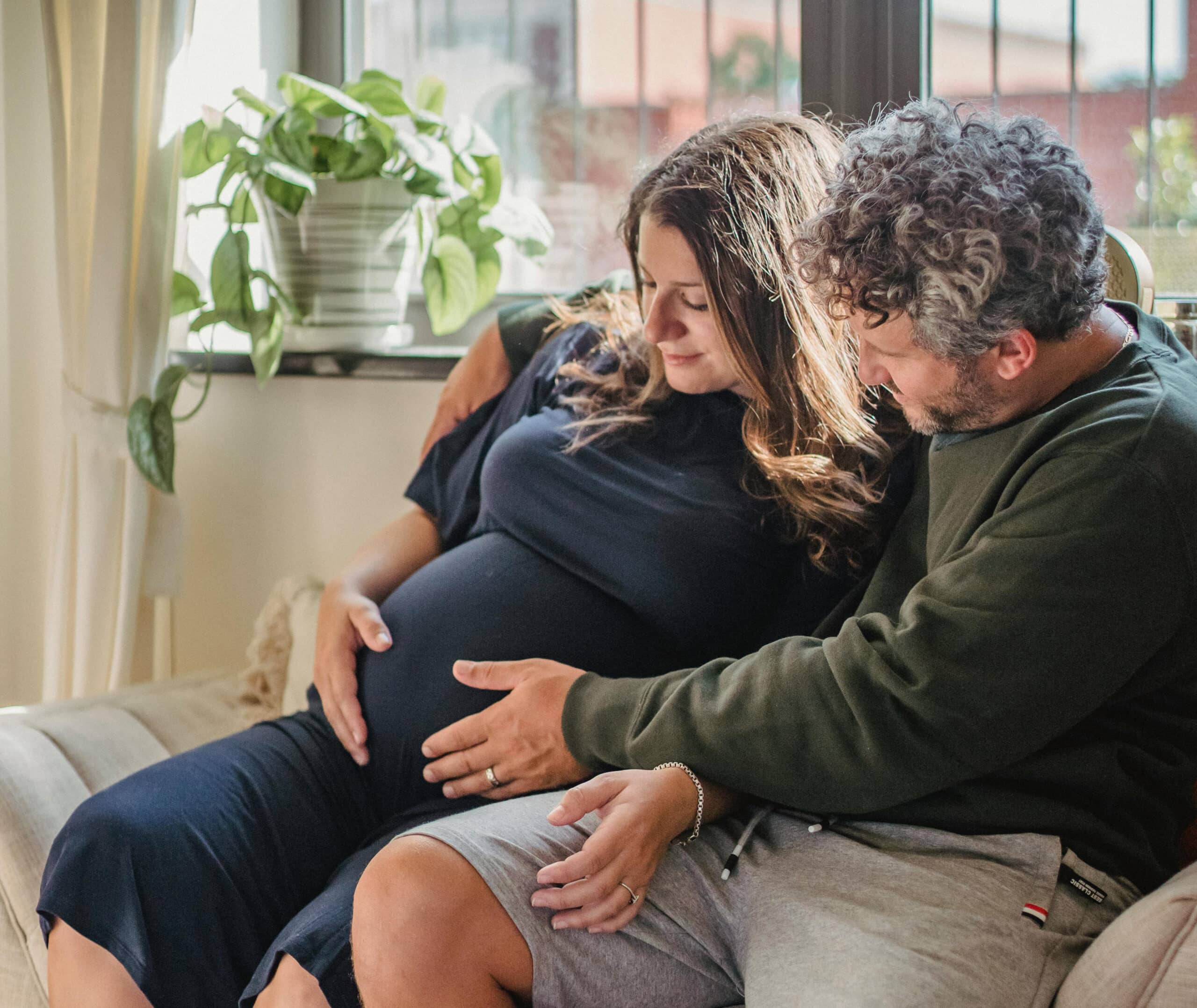 Pregnant woman and a man on a couch holding her pregnant belly