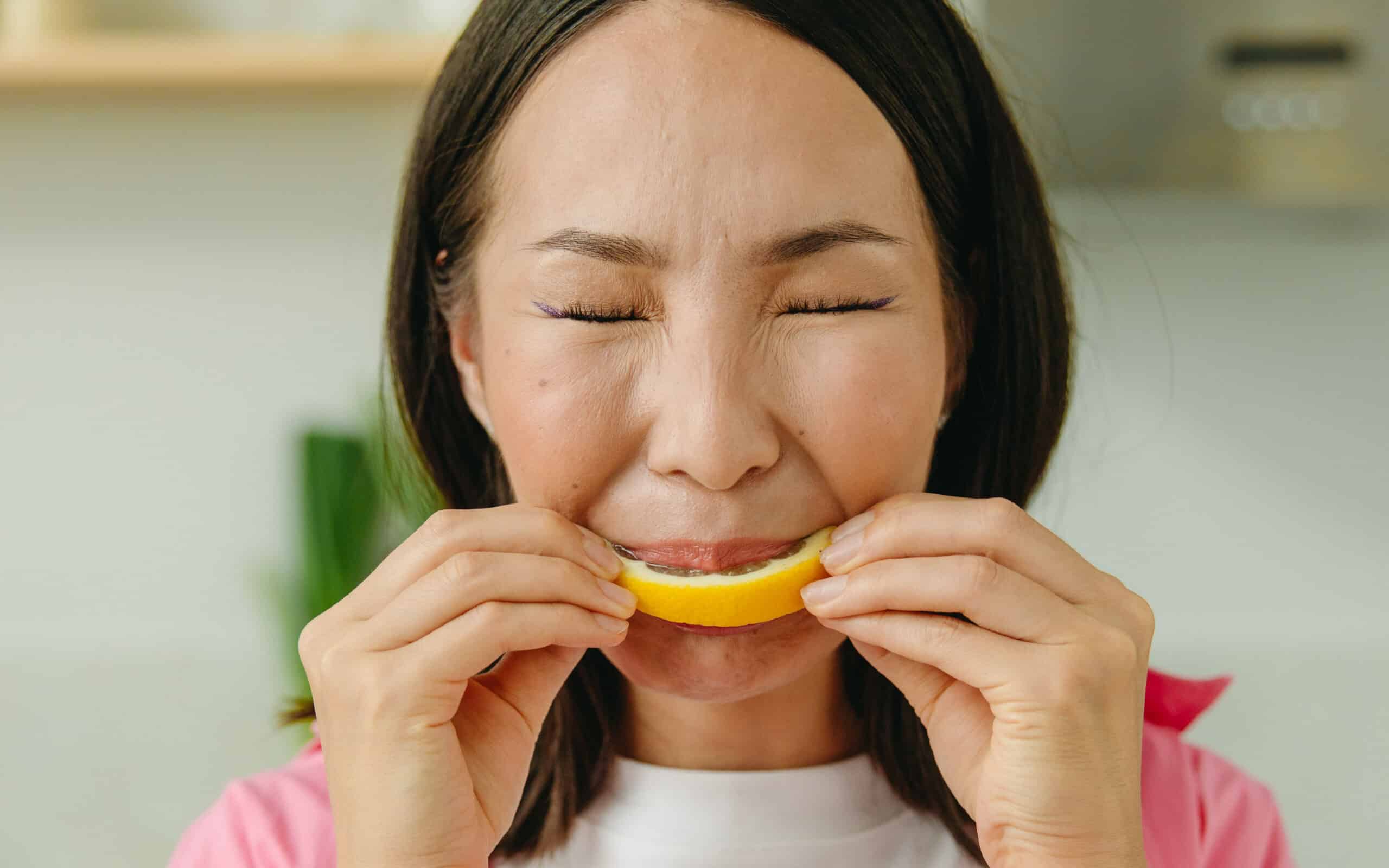 Woman wincing whilst biting into lemon slice