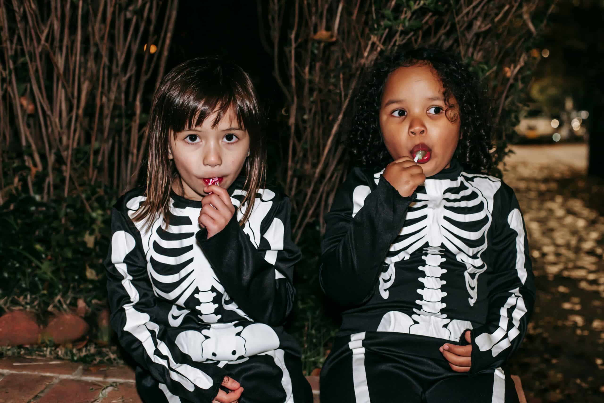 Two little girls in Halloween costumes, eating a sweet